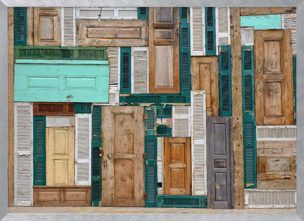 A framed art piece featuring a chaotic collage of various old, weathered wooden doors and window shutters arranged in a dense patchwork, showcasing a rustic texture and colors like natural wood, teal, green, and distressed white. Wall Art