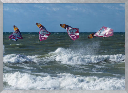 A composite, silver-framed photograph capturing the four stages of a windsurfer's impressive jump over choppy, white-capped ocean waves under a partly cloudy blue sky. Print