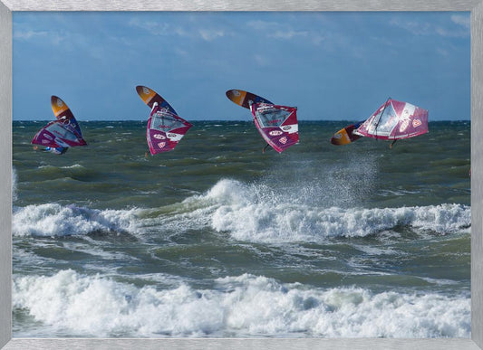 A composite, silver-framed photograph capturing the four stages of a windsurfer's impressive jump over choppy, white-capped ocean waves under a partly cloudy blue sky. Print