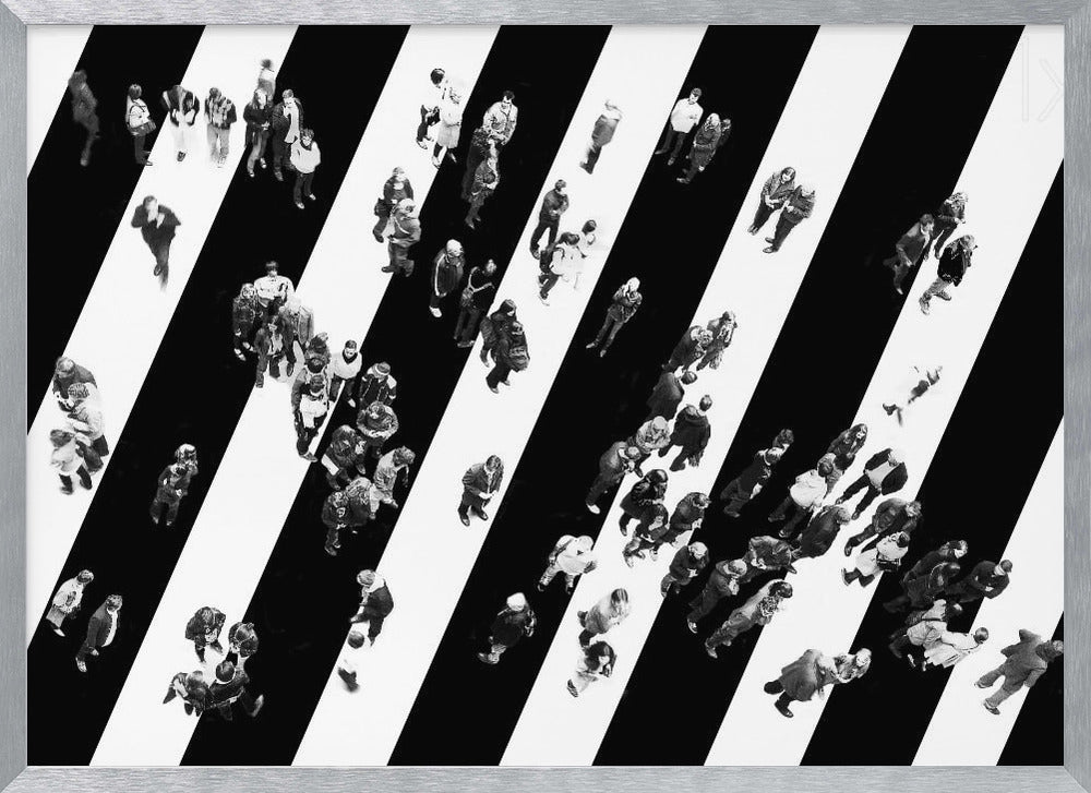 A striking black and white aerial photograph of dozens of people walking across a large, diagonally striped crosswalk. The high-contrast, graphic pattern of black and white stripes dominates the scene, with the small figures of pedestrians scattered across it, creating a sense of movement and urban anonymity. The image is presented within a simple silver frame. Print