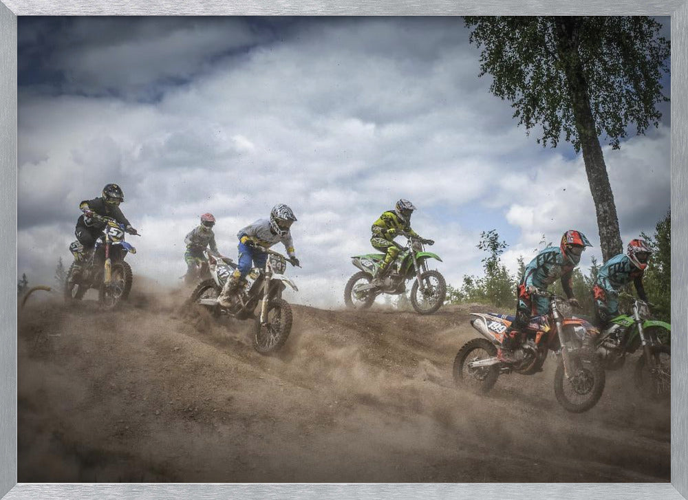 A dynamic action shot of several motocross riders racing up a dirt hill, kicking up a large cloud of dust. The riders are in full gear on colorful bikes, with a dramatic cloudy sky and a tall tree in the background. Print