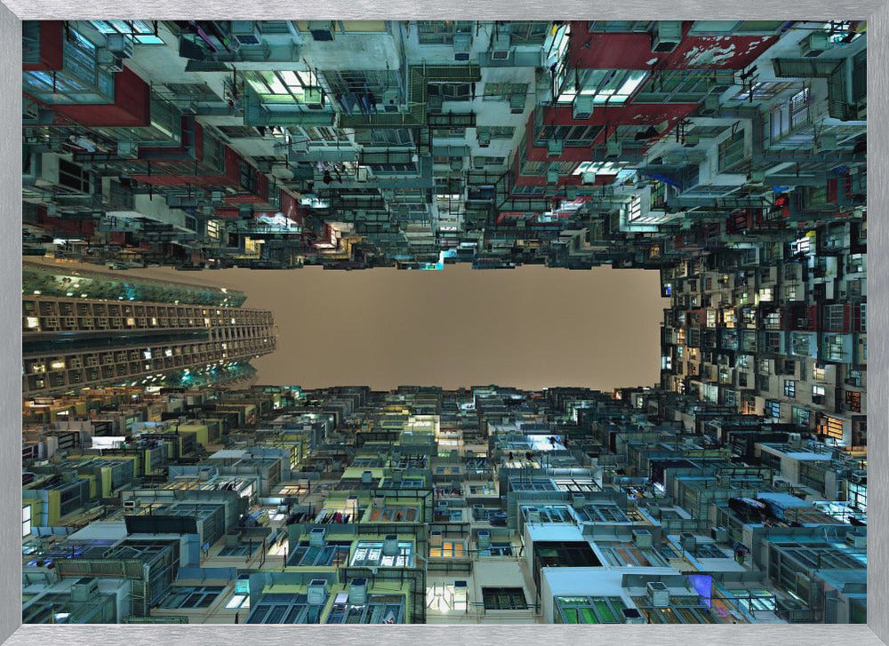 A framed, low-angle photograph looking up from a courtyard at densely packed, colorful apartment buildings that form a rectangle around a blank, overcast sky at night. Print