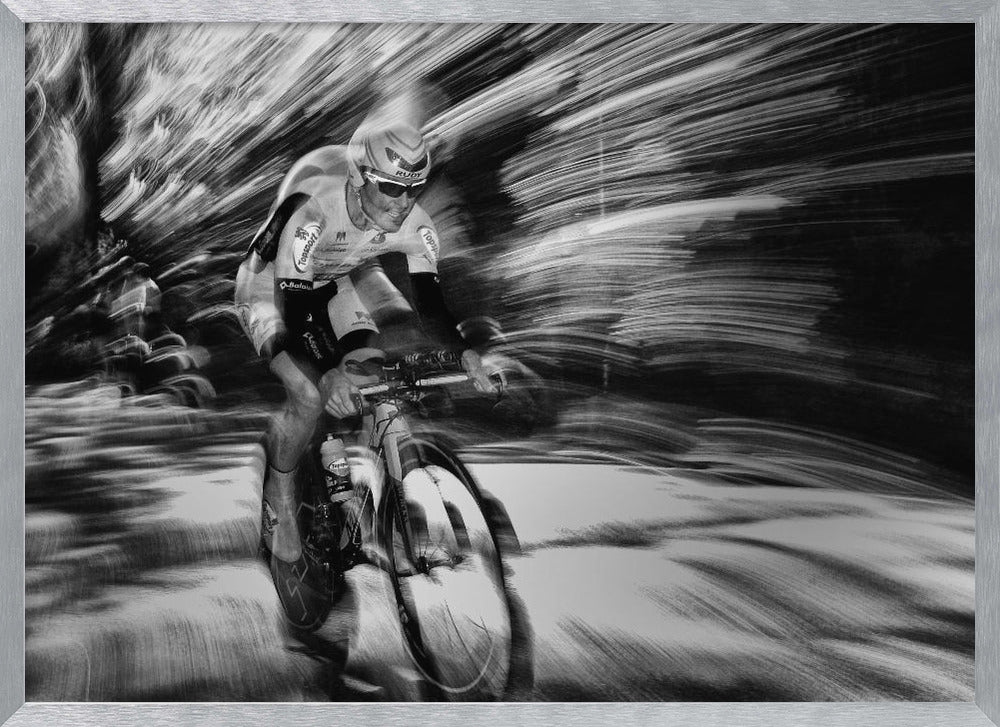 A dramatic black and white action shot of a professional cyclist racing. The cyclist is in focus, wearing a helmet and sunglasses, while the background is a streaky motion blur, creating a powerful sense of speed and movement. The image is enclosed in a silver frame. Wall Art