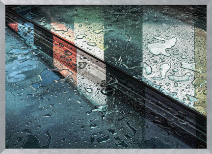 An abstract close-up photograph of a wet, dark surface, possibly a car, covered in raindrops, with a prominent black diagonal line. Colorful vertical stripes of red, cream, and green are reflected on the glossy, wet surface. The artwork is presented in a silver frame. Decor