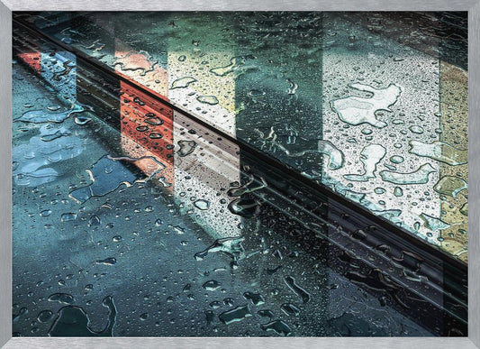An abstract close-up photograph of a wet, dark surface, possibly a car, covered in raindrops, with a prominent black diagonal line. Colorful vertical stripes of red, cream, and green are reflected on the glossy, wet surface. The artwork is presented in a silver frame. Decor