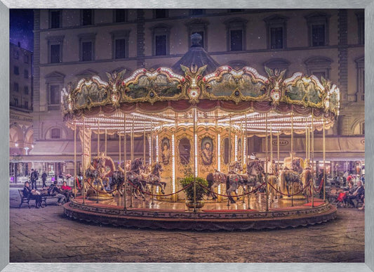 A beautifully illuminated vintage carousel with ornate horses in a European cobblestone plaza at night. The carousel is the central focus, glowing with warm lights against a backdrop of historic buildings and a starry purple sky. Poster