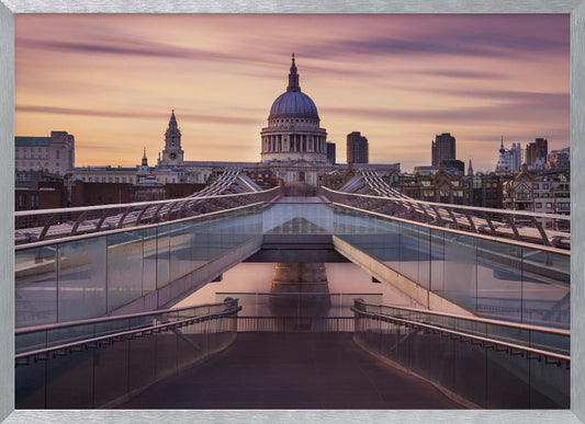 A photograph looking down the center of the Millennium Bridge in London, leading the eye directly to St. Paul's Cathedral, which is centered in the background under a beautiful purple and orange sunset sky. Print