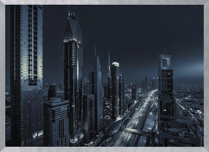A framed, blue-toned nighttime photograph of a futuristic city skyline from an elevated perspective, featuring illuminated skyscrapers and light trails from traffic on a major highway stretching into the distance. Poster