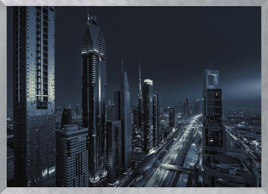 A framed, blue-toned nighttime photograph of a futuristic city skyline from an elevated perspective, featuring illuminated skyscrapers and light trails from traffic on a major highway stretching into the distance. Poster