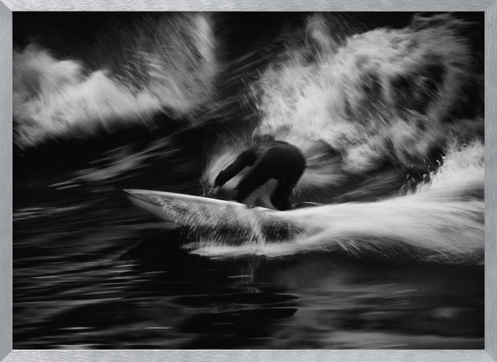A dynamic black and white action photograph of a surfer in a dark wetsuit, crouched low on a surfboard while riding a powerful wave. Motion blur captures the speed and energy of the moment, with white water spray exploding around the surfer against the dark ocean. Print