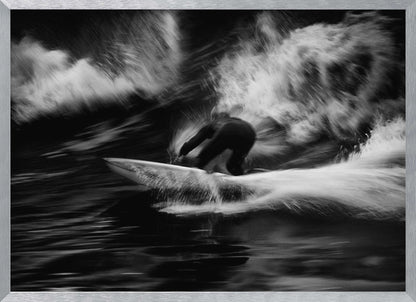A dynamic black and white action photograph of a surfer in a dark wetsuit, crouched low on a surfboard while riding a powerful wave. Motion blur captures the speed and energy of the moment, with white water spray exploding around the surfer against the dark ocean. Print