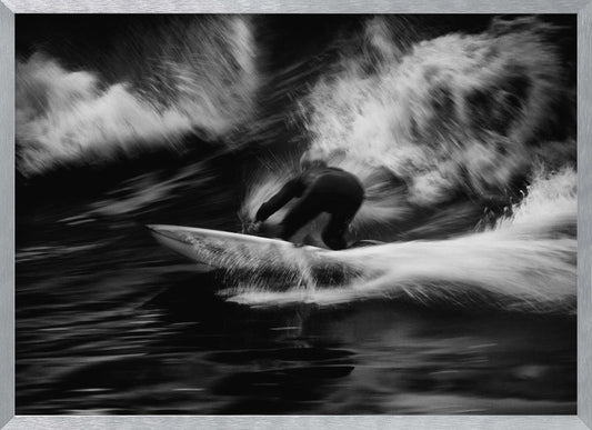 A dynamic black and white action photograph of a surfer in a dark wetsuit, crouched low on a surfboard while riding a powerful wave. Motion blur captures the speed and energy of the moment, with white water spray exploding around the surfer against the dark ocean. Print