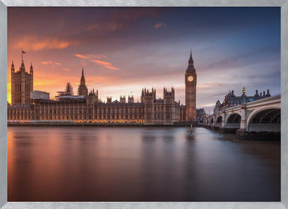 A framed photograph of the Houses of Parliament and Big Ben in London at sunset, with a dramatic orange and purple sky reflecting in the calm waters of the River Thames. Artwork