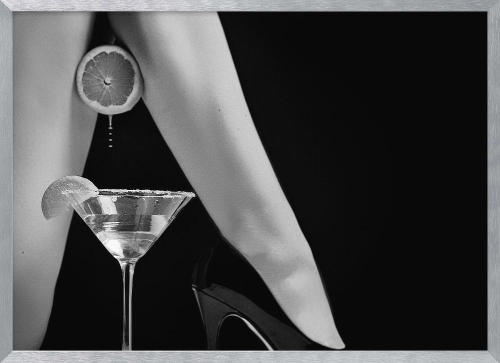 A framed, black and white photograph showing a woman's legs and a martini glass against a black background. A sliced citrus fruit is held between her thighs, with juice dripping towards the sugar-rimmed cocktail glass below. One foot is visible, wearing a black stiletto high heel. Artwork