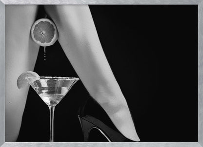 A framed, black and white photograph showing a woman's legs and a martini glass against a black background. A sliced citrus fruit is held between her thighs, with juice dripping towards the sugar-rimmed cocktail glass below. One foot is visible, wearing a black stiletto high heel. Artwork