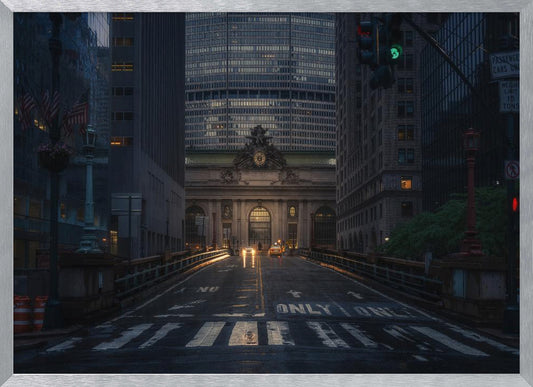 A moody photograph of a wet city street at dusk, leading towards the illuminated facade of Grand Central Terminal in New York City, which is framed by tall, modern skyscrapers. Decor