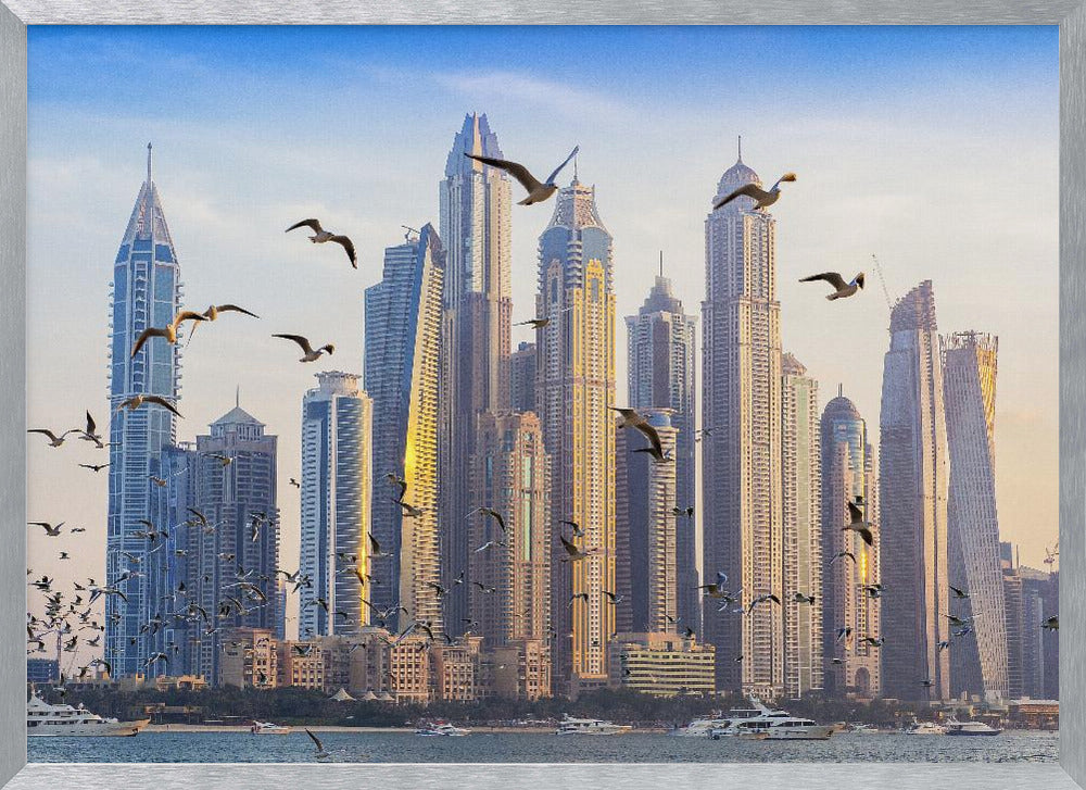A framed artwork of the Dubai city skyline, featuring modern skyscrapers bathed in the golden light of sunset. A flock of seagulls flies in the foreground above the water, where several yachts are docked. Artwork