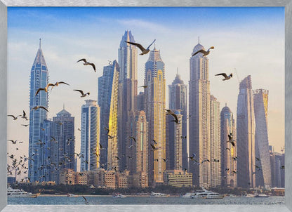 A framed artwork of the Dubai city skyline, featuring modern skyscrapers bathed in the golden light of sunset. A flock of seagulls flies in the foreground above the water, where several yachts are docked. Artwork