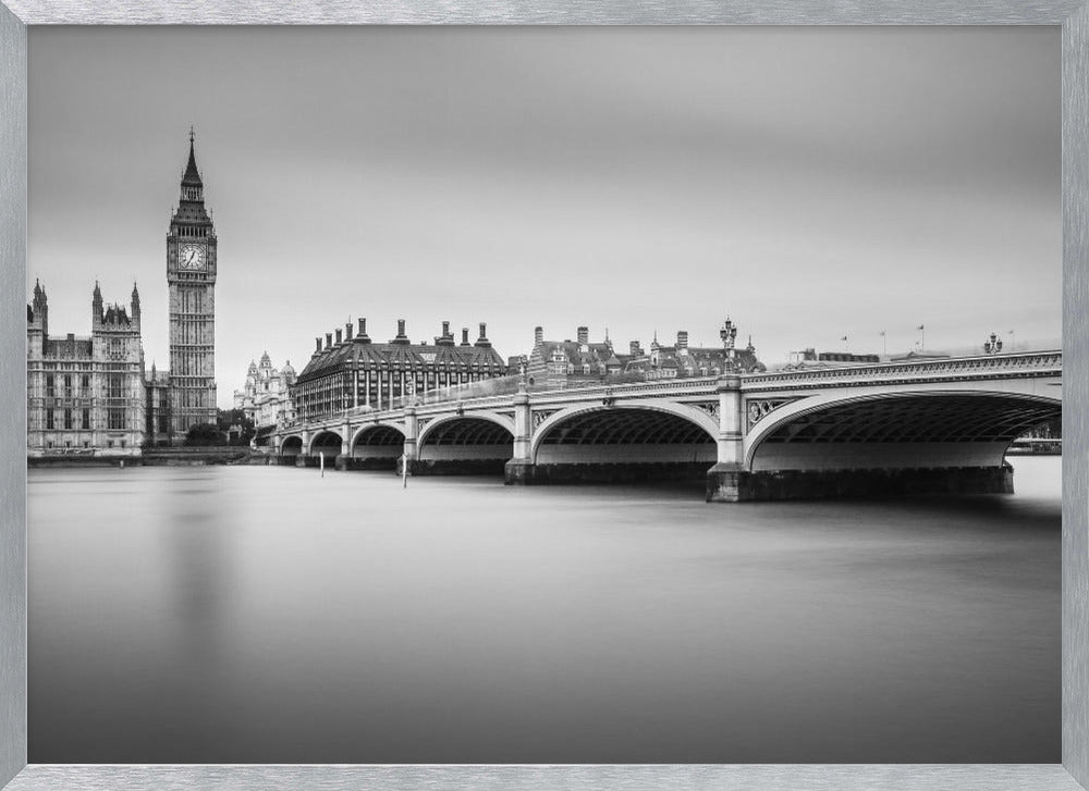 A black and white long-exposure photograph of the Elizabeth Tower (Big Ben) and the Houses of Parliament in London, viewed from across the River Thames. Westminster Bridge stretches across the frame over the smooth, milky water. The image is presented in a silver frame. Artwork