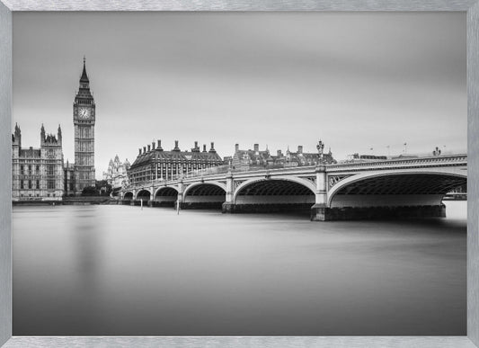 A black and white long-exposure photograph of the Elizabeth Tower (Big Ben) and the Houses of Parliament in London, viewed from across the River Thames. Westminster Bridge stretches across the frame over the smooth, milky water. The image is presented in a silver frame. Artwork