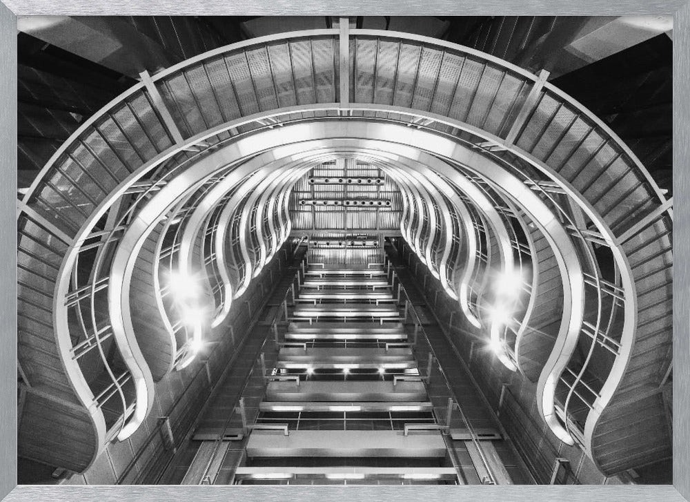 A symmetrical, low-angle black and white photograph of a futuristic escalator or grand staircase. The structure features illuminated, repeating curved arches on both sides, creating a tunnel-like perspective leading upwards. The image is presented within a silver-colored frame. Artwork