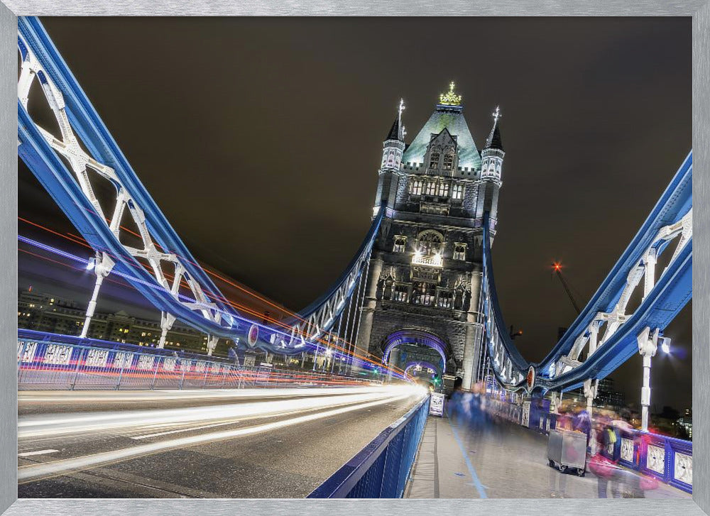 A dramatic, long-exposure night photograph from the deck of London's Tower Bridge, showing vibrant blue support structures curving towards an illuminated stone tower against a dark sky, with bright streaks of light from traffic. Wall Art