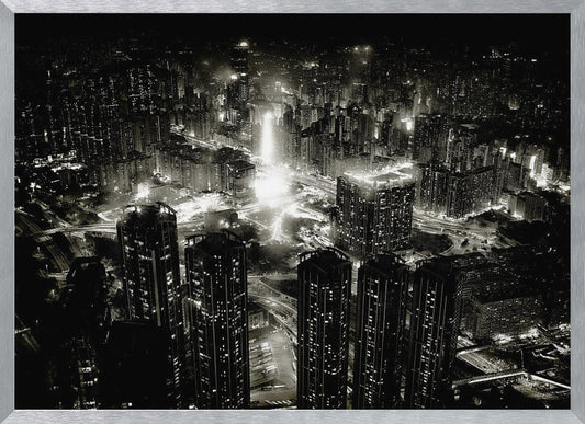 A framed black and white aerial photograph of a dense city at night. The high-angle view captures countless illuminated skyscrapers and winding highways, creating a dramatic and bustling urban landscape. Print