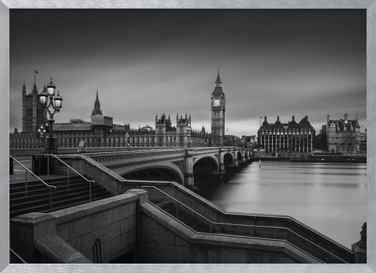 A framed, black and white, long-exposure photograph of the London skyline featuring the Houses of Parliament and the Big Ben clock tower across the River Thames. In the foreground, stone steps lead down towards Westminster Bridge, and the water of the river is smooth and reflective under a dark, cloudy sky. Print