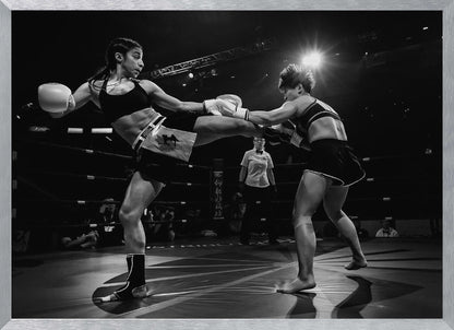 A dramatic black and white action photograph of two female kickboxers in a ring. One fighter, airborne, executes a high kick that connects with the other fighter's gloves, who is bracing for the impact. A referee stands in the background under bright arena lights. Poster