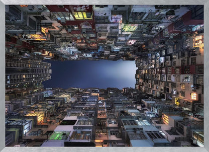 A striking low-angle photograph looking up from a narrow courtyard at the night sky, completely framed by towering, densely packed, and weathered apartment buildings with glowing windows, creating a sense of urban enclosure. Decor