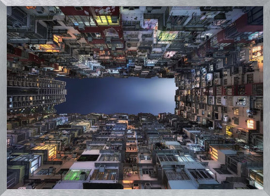 A striking low-angle photograph looking up from a narrow courtyard at the night sky, completely framed by towering, densely packed, and weathered apartment buildings with glowing windows, creating a sense of urban enclosure. Decor