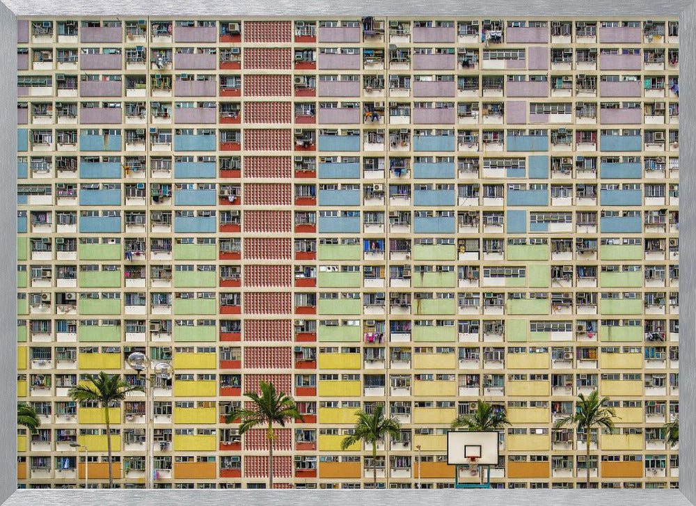 A symmetrical, frontal photograph of the colorful Choi Hung Estate in Hong Kong, featuring a massive grid of apartments with balconies painted in a rainbow of pastel colors including purple, blue, green, yellow, and orange. Palm trees and a basketball court are visible at the base of the building, which is enclosed in a silver frame. Wall Art