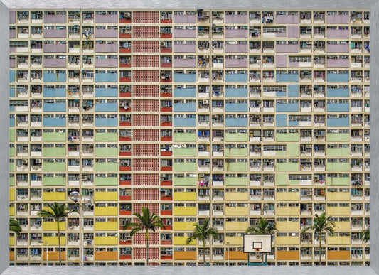 A symmetrical, frontal photograph of the colorful Choi Hung Estate in Hong Kong, featuring a massive grid of apartments with balconies painted in a rainbow of pastel colors including purple, blue, green, yellow, and orange. Palm trees and a basketball court are visible at the base of the building, which is enclosed in a silver frame. Wall Art