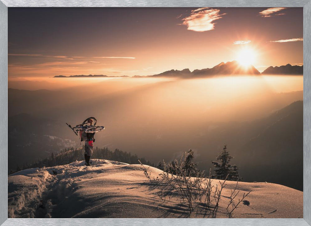 A lone person stands on a snowy mountain peak at sunrise, carrying a bicycle over their shoulder. They look out over a valley filled with a sea of clouds, with distant mountain ranges silhouetted against the bright, golden sun. Artwork