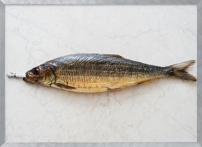 A surreal photograph of a whole smoked fish with a cigarette butt in its mouth, laying horizontally on a white marble surface, all within a silver frame. Wall Art