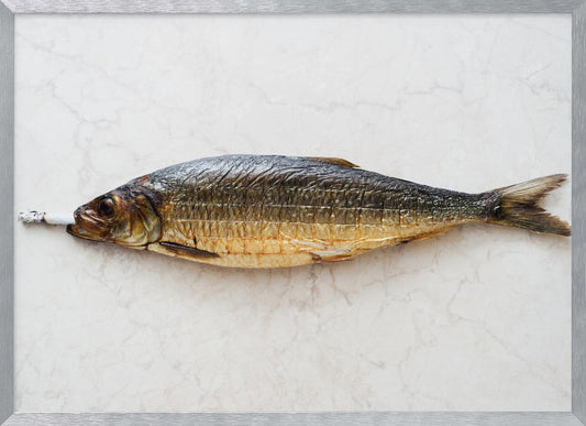 A surreal photograph of a whole smoked fish with a cigarette butt in its mouth, laying horizontally on a white marble surface, all within a silver frame. Wall Art