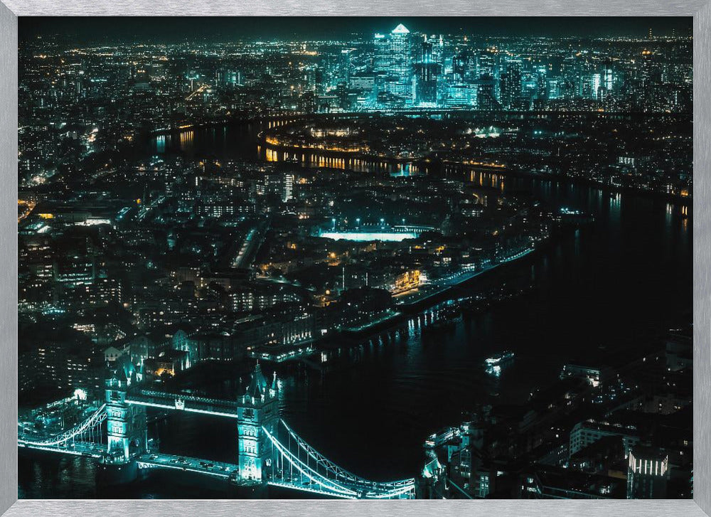 A framed aerial photograph of London at night, featuring the iconic Tower Bridge illuminated in bright teal in the foreground and the glowing skyscrapers of Canary Wharf across the River Thames in the background. Artwork