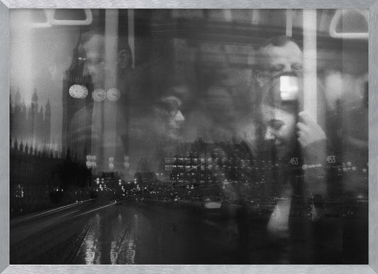 A moody black and white double exposure photograph showing a rainy London street at night with Big Ben, overlaid with the faint reflections of people inside a moving vehicle like a bus. The image has a dreamy, layered effect and is displayed in a silver frame. Print