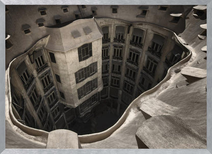 A surreal, high-angle photograph looking down into the distorted, cavernous courtyard of a building. The walls and windows appear to melt and curve inwards towards a dark void, creating a powerful optical illusion. The image has a muted, sepia-toned color palette and is presented in a silver frame. Wall Art