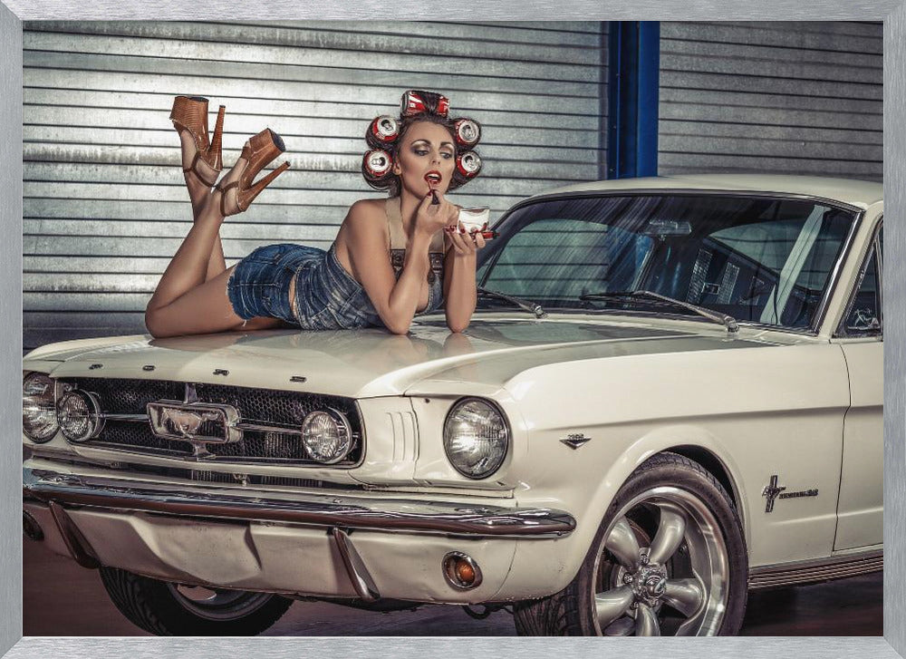A woman in a retro pin-up style lies on the hood of a vintage white Ford Mustang in a garage, applying red lipstick with her hair set in soda can curlers. Poster