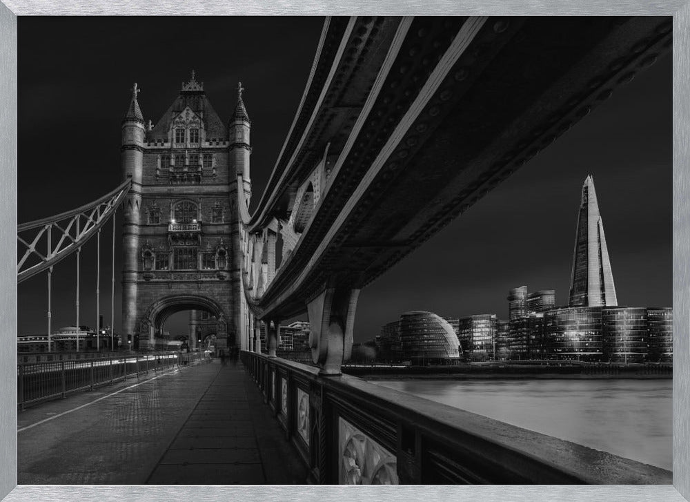 A dramatic, low-angle black and white photograph of London's Tower Bridge at night, taken from the pedestrian walkway. The image showcases the architectural details of the bridge and the illuminated modern city skyline, including The Shard, across the River Thames. Print