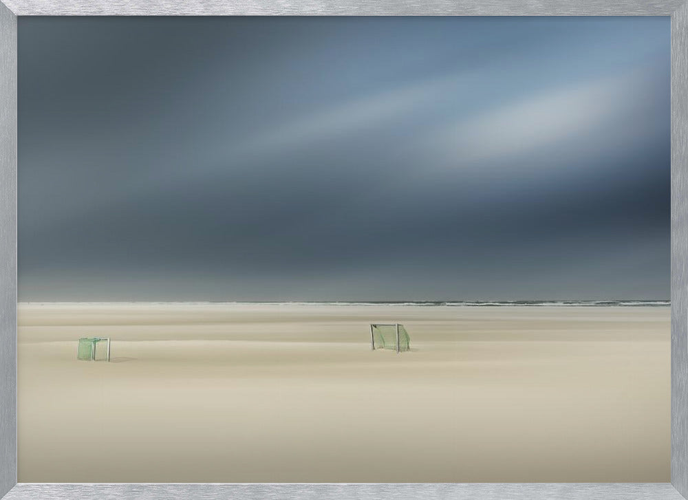 A minimalist long-exposure photograph of a vast, empty beach under a dark, moody sky. Two small, solitary soccer goals sit on the pale sand, with the ocean visible as a thin line in the distance. The artwork is presented in a silver frame. Artwork