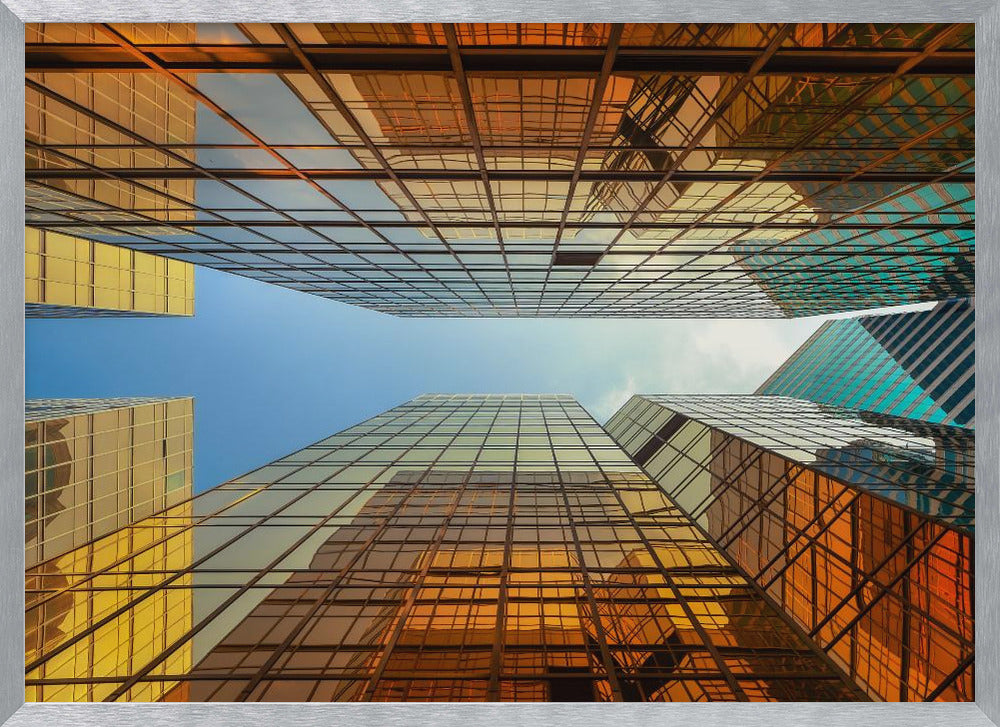 A low-angle, upward view of modern skyscrapers with golden reflective glass windows, creating a geometric pattern against a narrow strip of clear blue sky. Decor