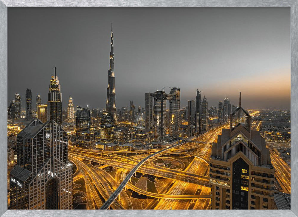 A framed, high-angle, long-exposure photograph of the Dubai skyline at dusk. The towering Burj Khalifa stands out against a grey sky, while the city's skyscrapers are illuminated. In the foreground, a complex network of highways glows with the yellow light trails of traffic, creating intricate patterns. Poster