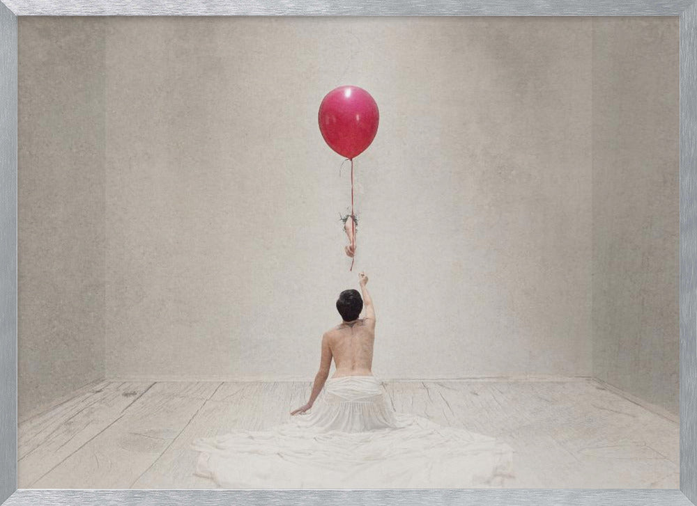 A surreal fine art photograph of a person with a bare back and a long white skirt, sitting on the floor of a minimalist grey room. They are reaching up towards a small figure hanging from the string of a large, bright red balloon that floats towards the ceiling. The image is enclosed in a silver frame. Artwork
