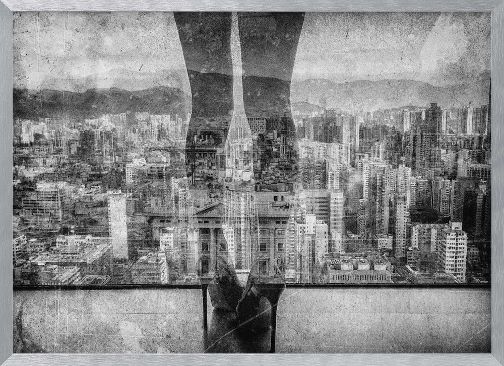 A framed, black and white artistic photograph featuring a double exposure. A vast, dense cityscape with distant mountains is visible through the translucent silhouette of a person's legs standing on a balcony edge. Poster