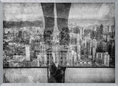 A framed, black and white artistic photograph featuring a double exposure. A vast, dense cityscape with distant mountains is visible through the translucent silhouette of a person's legs standing on a balcony edge. Poster