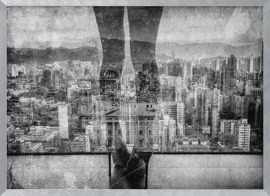 A framed, black and white artistic photograph featuring a double exposure. A vast, dense cityscape with distant mountains is visible through the translucent silhouette of a person's legs standing on a balcony edge. Poster