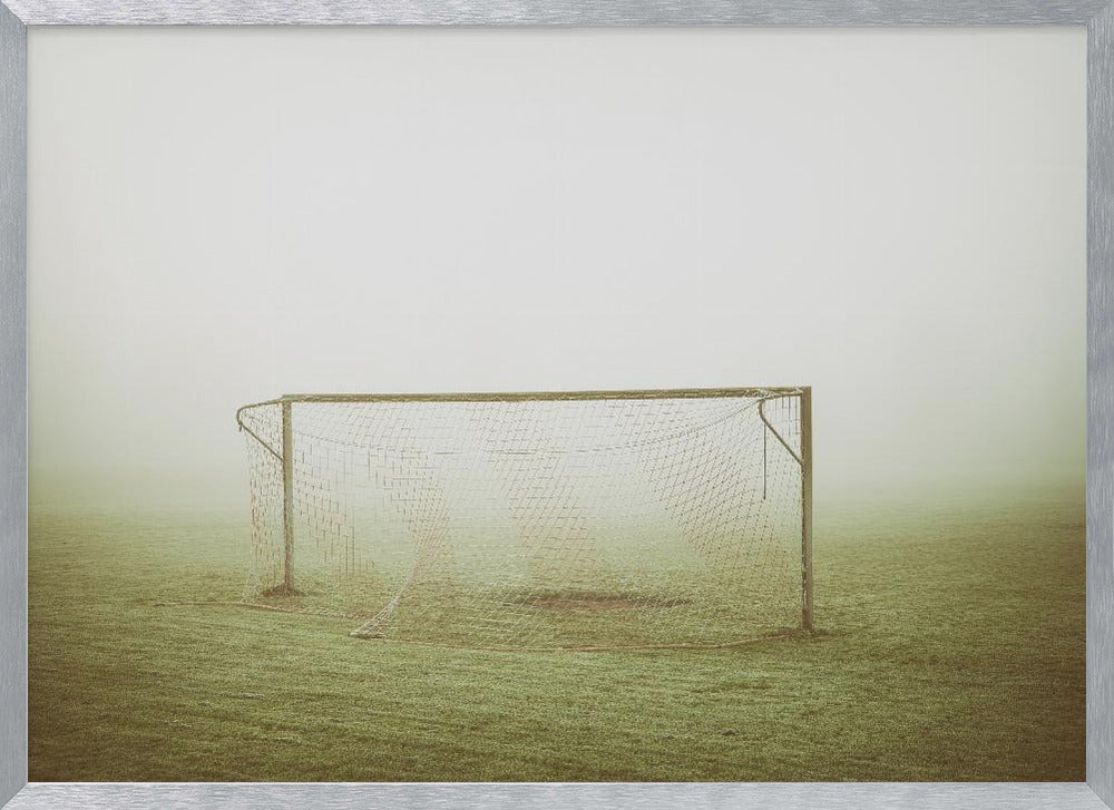 A framed photograph of an empty soccer goal with a net, standing alone on a green grass field enveloped in thick, white fog, creating a minimalist and atmospheric scene. Poster