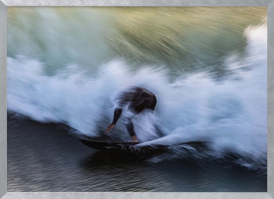An abstract, motion-blur photograph of a surfer in a black wetsuit, crouched on their board and surrounded by a dynamic swirl of white sea spray and dark blue water, all enclosed in a silver frame. Artwork